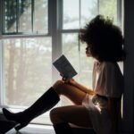 A woman enjoys a peaceful reading session by a window, bathed in natural light.